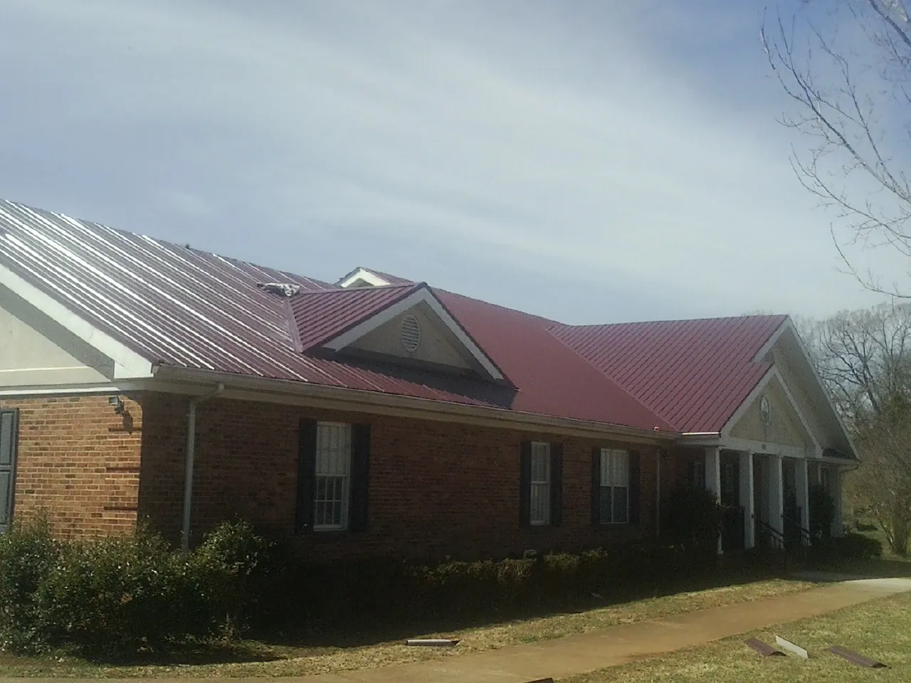 Red metal roof with gabled entries on a long brick building, from a Hail Damage Roof Repair job in Toledo